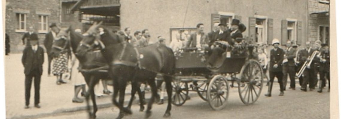 Das Foto zeigt einen Ausschnitt vom 1. Feuerwehrfest im Jahr 1947. Links: Haus Wienand, rechts: Haus Pfeuffer. Rechts neben der Kutsche mit Helm: August Rachor. In der Kutsche mit Zylinder: Andres Reuter