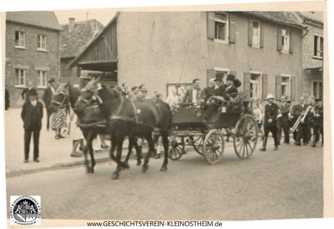 Das Foto zeigt einen Ausschnitt vom 1. Feuerwehrfest im Jahr 1947. Links: Haus Wienand, rechts: Haus Pfeuffer. Rechts neben der Kutsche mit Helm: August Rachor. In der Kutsche mit Zylinder: Andres Reuter