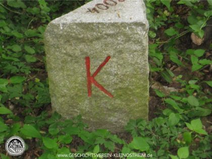 Das Foto zeigt einen so genannten Dreimärker mit den Buchstaben K, D und M. Der Dreimärker zeigt an, dass hier die Gemarkungen von Kleinostheim, Damm und Mainaschaff aneinanderstoßen. Bei den regelmäßigen Grenzbegehungen der Feldgeschworenen werden die Grenzsteine kontrolliert.