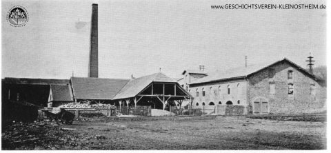 Das Foto zeigt die Tonwarenfabrik Geiger & Goller in der Nähe des Bahnhofs. Sie wurde 1884 gegründet und fertigte Ziegelsteine (Blendsteine). 1936 wurde sie verkauft und nach Mainflingen verlegt. Nachdem im Krieg hier russische Kriegsgefangene untergebracht waren, ließ die Gemeinde das Gebäude renovieren, in dem sich dann ab 1950 die Strumpffabrik Lasea niederließ.