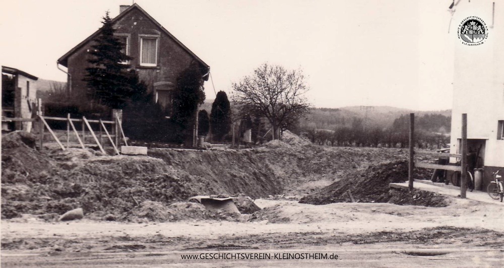 Das heutige Foto zeigt einen Ausschnitt vom Beginn der Kanalisation des Steinbachs von der B 8 bis zur Bahnlinie in den 60er Jahren. Bis dahin floss der Bach teilweise noch offen durch den Ort, wobei es gelegentlich zu Überschwemmungen kam. Da der Beschdamper (die Brücke des Steinbachs über die Eisenbahn) wegen des Baus der Oberleitung abgerissen werden musste und der Bach unter der Bahn durchgeführt wurde, lag es nahe, auch den restlichen Lauf zu kanalisieren.