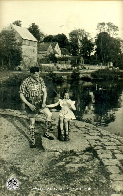 Das Foto von 1953 zeigt Menschen am Fischerbau. Der Fischerbau war eine Art natürliches Hafenbecken für die Fischer. Hier konnte man die Fischer beim Waschen ihrer Netze und dem Trocknen auf der angrenzenden Wiese sehen. Der Fischerbau verschwand durch den Bau der neuen Schleuse Ende der 60er Jahre, weil der Wasserstand nun zwei Meter höher war als vorher.