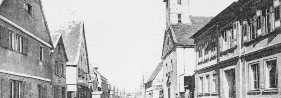 Die Ansichtskarte von 1920 zeigt einen Ausschnitt aus der Hauptstraße. Man sieht rechts die alte Schule, dahinter die Laurentiuskirche. Autos waren eher selten zu sehen.