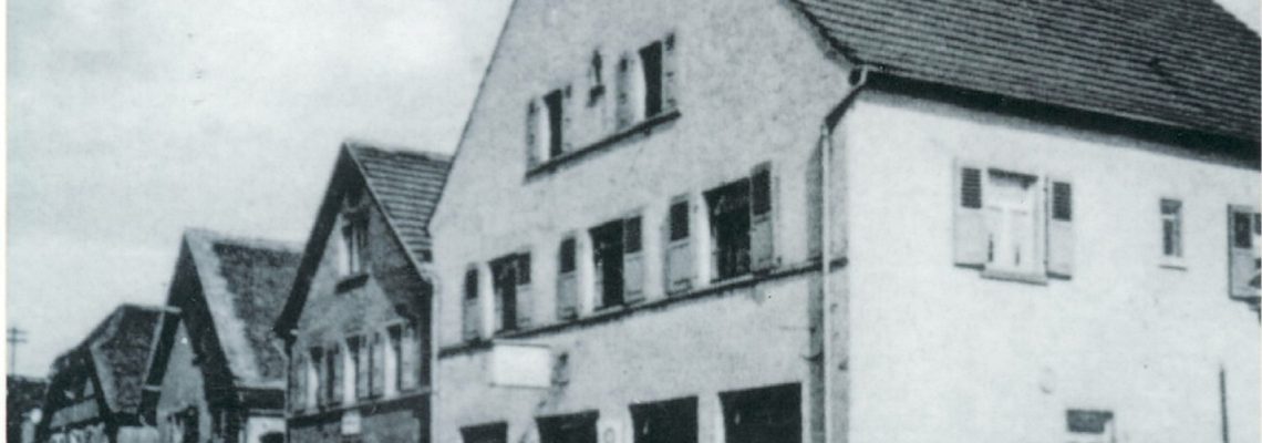 Das Foto zeigt das Gasthaus zum Engel im Jahre 1939. Erster Engelwirt war seit 1831 Peter Christ. Nach ihm folgten 1867 Johann Leitz, 1898 Johann Nikolaus Leitz und 1929 Cornelius Leitz. Der Saal hinter dem „Engel“ war erst Tanzsaal, dann in den 50er und frühen 60er Jahren das einzige Kino Kleinostheims (Gloria Lichtspiele). In den letzten Jahren hat sich der Name der Gaststätte wiederholt geändert.