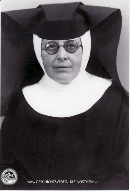 Das Foto zeigt Schwester Barbara Fries (1886 – 1951). Sie war Krankenschwester der Dillinger Franziskanerinnen und zwischen 1922 und 1951 in der ambulanten Krankenpflege in Kleinostheim tätig. Für ihre Leistungen wurde sie 1951 zur Ehrenbürgerin ernannt. Die Barbarastraße erinnert noch heute an sie.