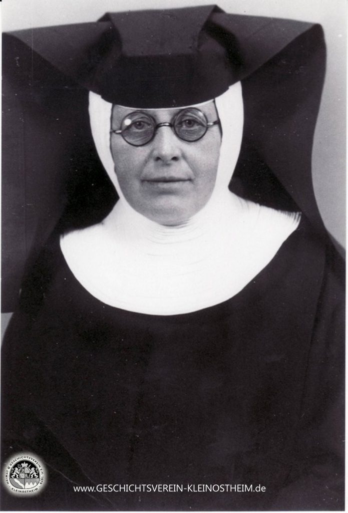 Das Foto zeigt Schwester Barbara Fries (1886 – 1951). Sie war Krankenschwester der Dillinger Franziskanerinnen und zwischen 1922 und 1951 in der ambulanten Krankenpflege in Kleinostheim tätig. Für ihre Leistungen wurde sie 1951 zur Ehrenbürgerin ernannt. Die Barbarastraße erinnert noch heute an sie.