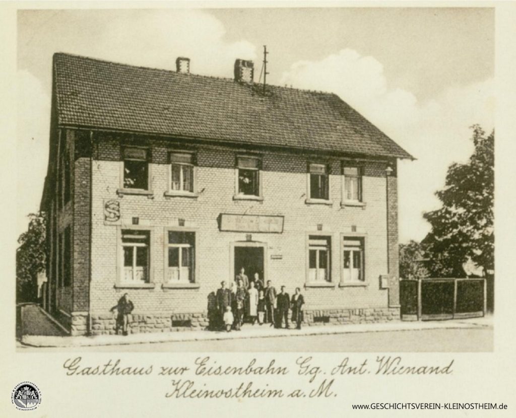 Das Foto aus dem Jahr 1940 zeigt das Gasthaus zur Eisenbahn, ab ca. 1968 auch bekannt unter dem Namen Cille-August.
Gegründet wurde es 1906 von Cäcilie und Georg Wienand. Später bekam es den Namen „Kleinostheimer Hof“. 2020 wurde es geschlossen.