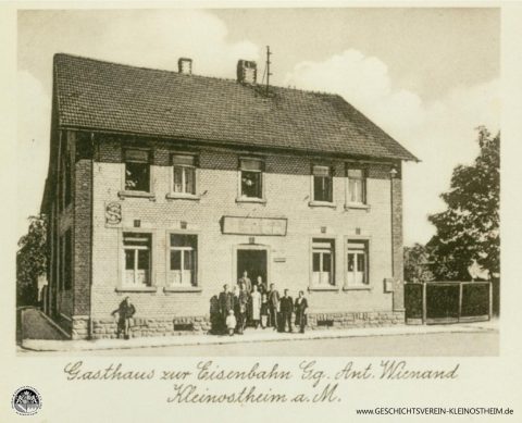 Das Foto aus dem Jahr 1940 zeigt das Gasthaus zur Eisenbahn, ab ca. 1968 auch bekannt unter dem Namen Cille-August. Gegründet wurde es 1906 von Cäcilie und Georg Wienand. Später bekam es den Namen „Kleinostheimer Hof“. 2020 wurde es geschlossen.