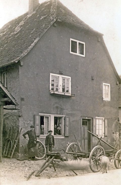 Das Foto zeigt die Schmiede Leibacher in der heutigen Hanauer Straße etwa um 1911/12. Am Fenster sieht man Gregor Leibacher mit Frau, im Fenster daneben seine Tante. Vor dem Haus stehen Georg und Emil Leibacher.